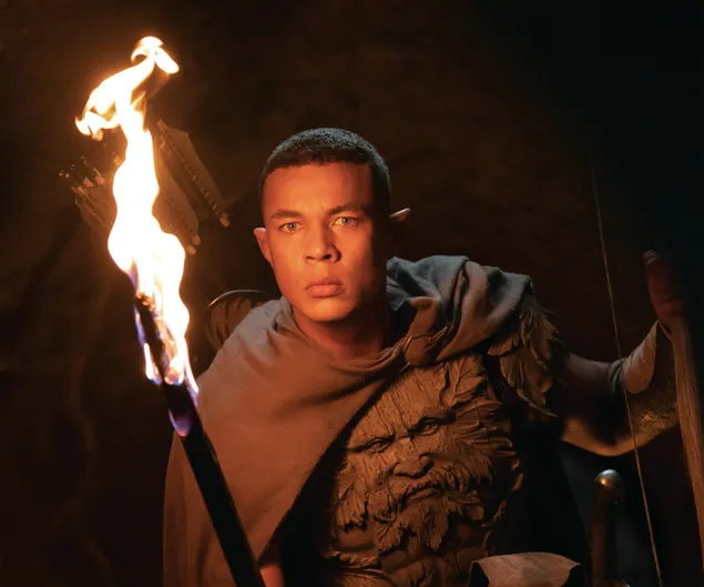 Mann in Umhang und Anzug mit feurigem Baum aus der Serie „Herr der Ringe: Rings of Power“. 2K Hintergrundbild