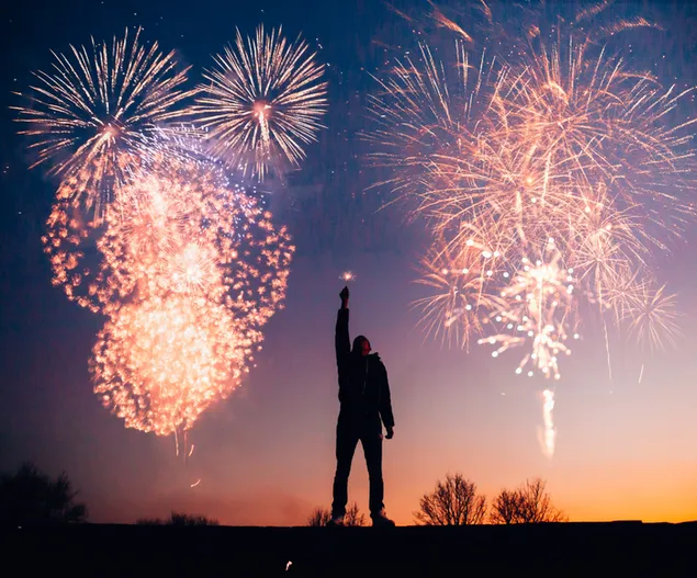 Man's silhouette holding a firecracker with amazing fireworks display background