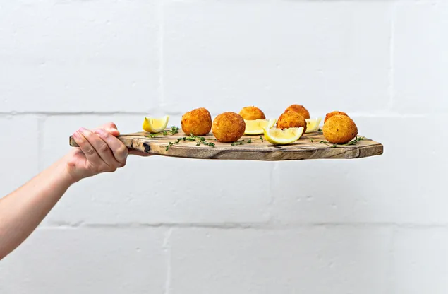 Manos sosteniendo una tabla de cortar de madera con bolas de queso con rodajas de limón