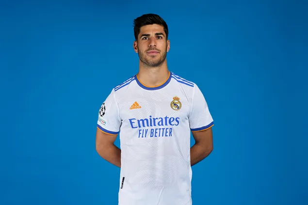 Marco Asensio posa con las manos a la espalda frente a un fondo azul con la camiseta del Real Madrid