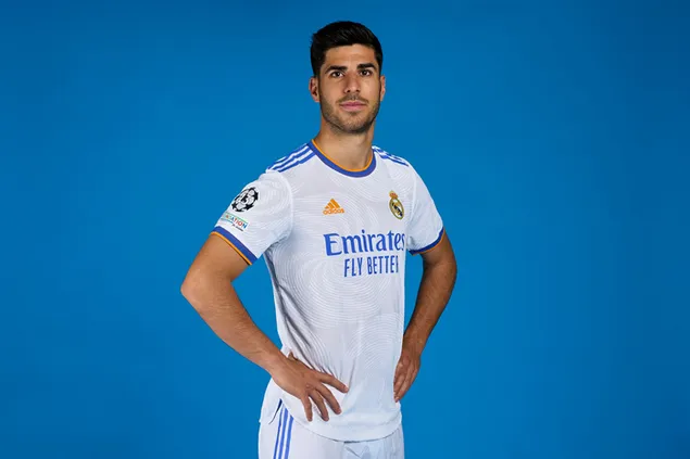 Marco Asensio posa con las manos en las caderas frente a un fondo azul con la camiseta del Real Madrid