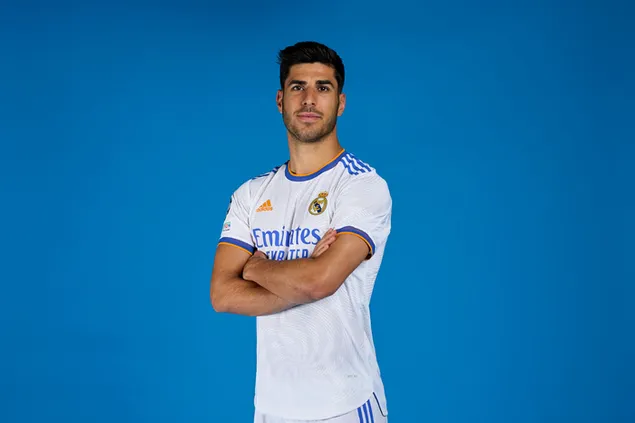 Marco Asensio poses with hands folded in front of a blue background wearing a Real Madrid jersey