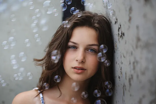Mesmerizing blue eyes of a brunette young girl with floating bubbles background 