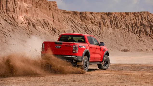 Mobil Ford Ranger Raptor 2022 tampak belakang dan samping meninggalkan debu dengan paninaj saat berkendara di padang pasir unduhan