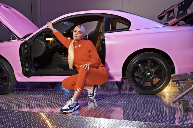 Model Kylie Jenner draagt ​​oranje adidas naast een roze auto