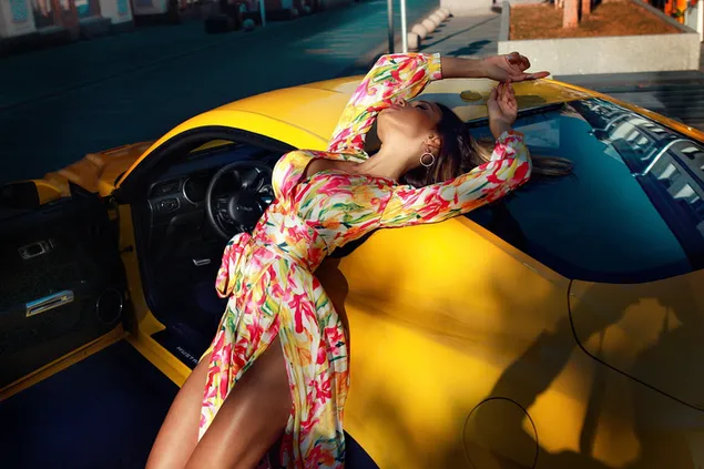 Modelo con un vestido largo artístico posando en coche amarillo