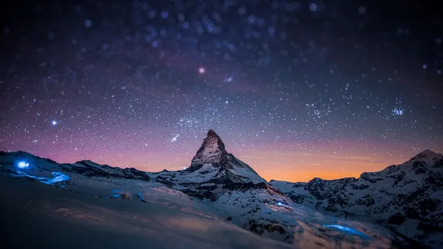 Montañas nevadas bajo las estrellas y el cielo coloreado por el sol poniente