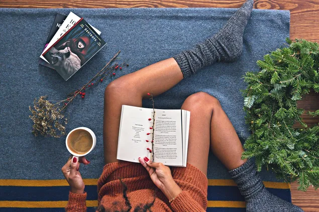 Morena girl reading books and coffee in hand with wreath and holly nearby 