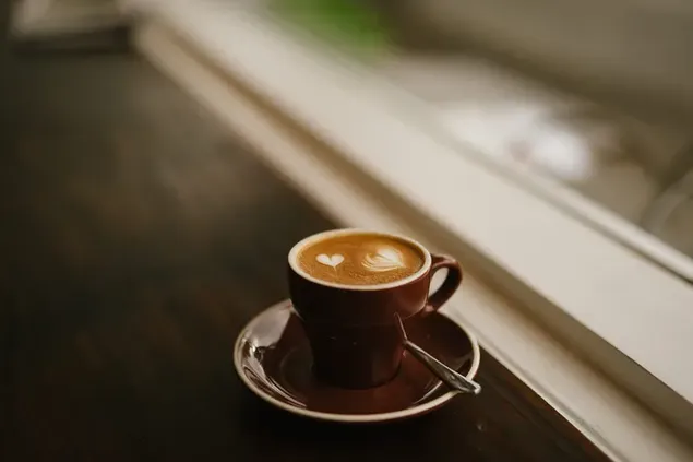 Café de la mañana con un arte de corazón en una pequeña taza marrón