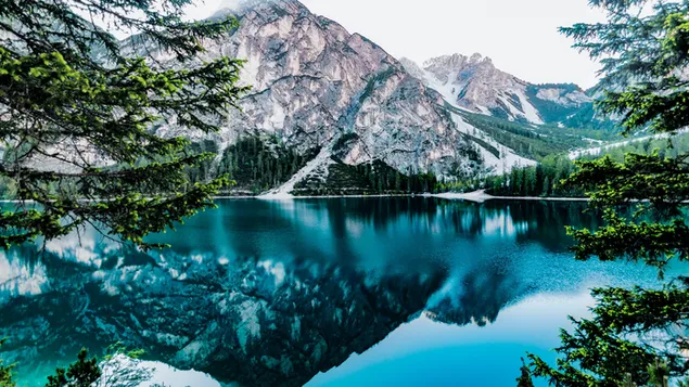 Montañas, árboles y picos nevados reflejados en un cielo nublado y agua clara del lago 4K fondo de pantalla