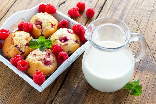 Muffins de frambuesa y una jarra de leche en una mesa de madera