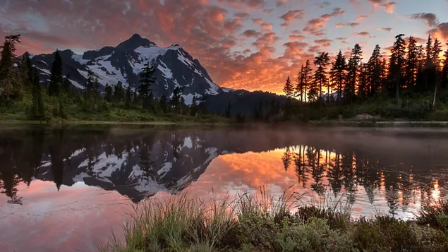 Reflejo natural de montañas nevadas y siluetas de árboles en el agua al amanecer. 4K fondo de pantalla