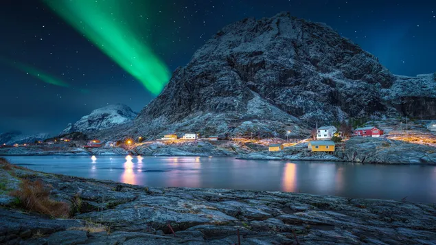 Пейзаж на северното сияние със заснежени скали и къщи, отразени в реката 4K тапет