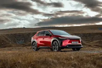 흙바닥에 마른 식물 사이에 주차된 붉은색 Toyota bz4x 자동차의 흐린 전망 4K 배경화면