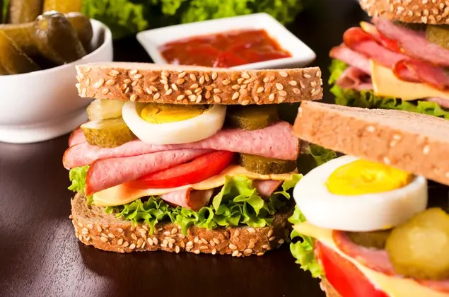 Sandwich clubhouse roti gandum yang berlebihan dengan ham dan telur rebus