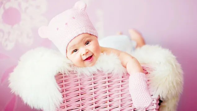 Foto af sød baby med vanter og hue fotograferet i håndlavet lyserød kurv