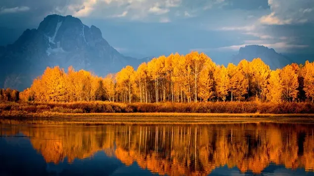 Picos de montaña que llegan a las nubes y árboles de otoño reflejados en el lago