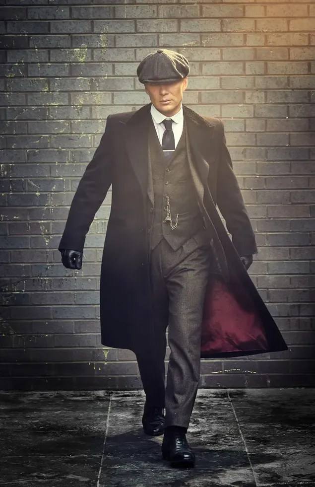 Porträt des Charakters der Fernsehserie Peaky Blinders mit langem Mantel und Anzug vor der Wand herunterladen