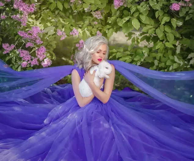 ピンクの花の中で白いウサギと紫のドレスで美しいモデルの女の子のポーズ