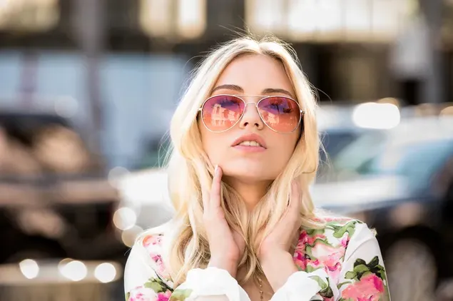 Поза плавуше у цветној хаљини са рукама на бради испред аутомобила на мутној уличној позадини 4K позадина