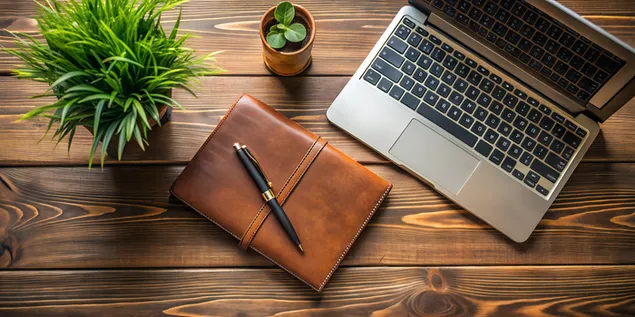 革製ノートブック、洗練されたペン、ミニマリストなラップトップ、磨かれた木製デスクを備えたプレミアムワークスペースのトップダウンビュー 4K 壁紙