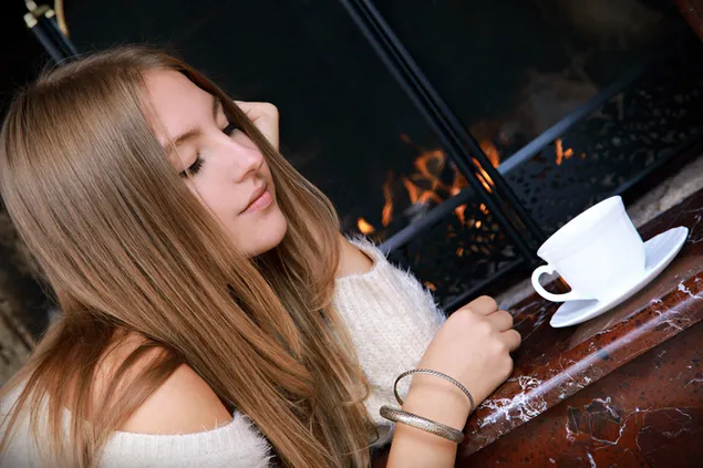Pretty petite brunette girl having coffee by the fireplace download