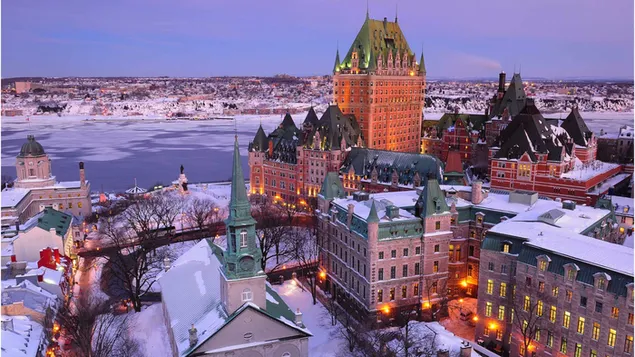 Ciutat del Quebec amb aigua gelada del llac al costat d'estructures arquitectòniques amb torres i edificis sota la neu 4K fons de pantalla