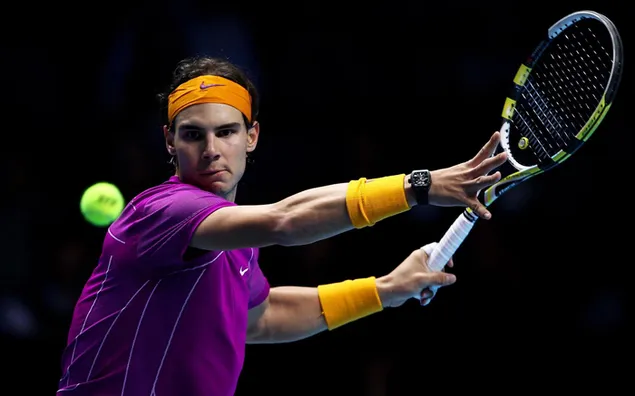 Rafael Nadal lila T-Shirt mit orangefarbenen Handgelenken, bevor er den Ball vor schwarzem Hintergrund trifft