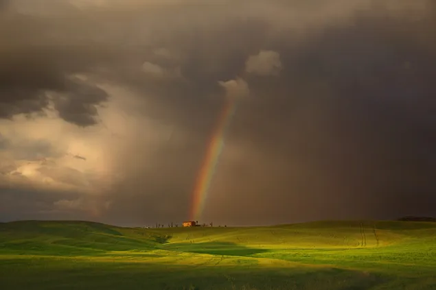 Regenboog die uit de lucht neerdaalt naar het grasveld tussen de regenwolken
