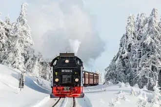 Красно-черный паровоз движется по железной дороге среди заснеженных деревьев 2K обои