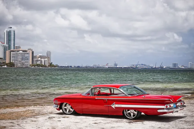 Red chevrolet impala next to sea view buildings download