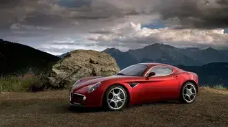 Tapeta Červené sportovní auto Alfa Romeo s ocelovými koly zaparkované na polní cestě mezi horami za oblačného počasí 4K