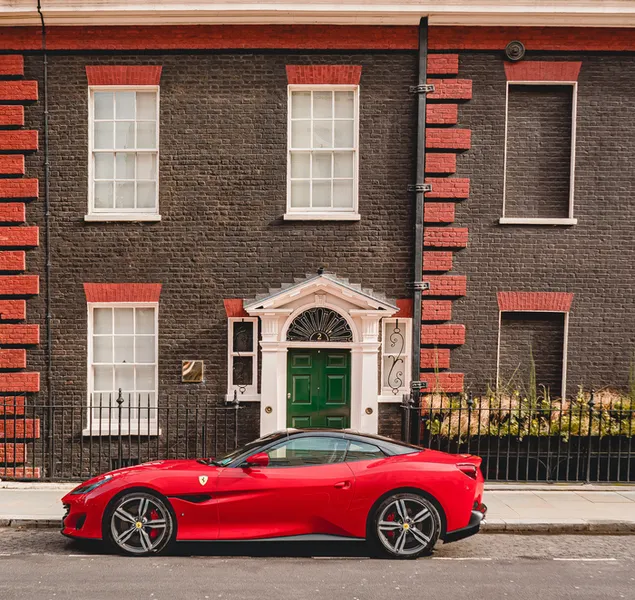 Raudona kupė stovi šalia rudų plytų pastato 2K ekrano užsklanda