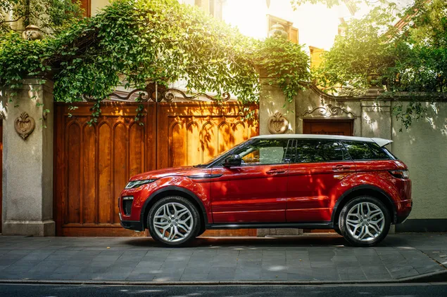 Rode Range Rover Evoque voor een poort met wijnranken 4K achtergrond
