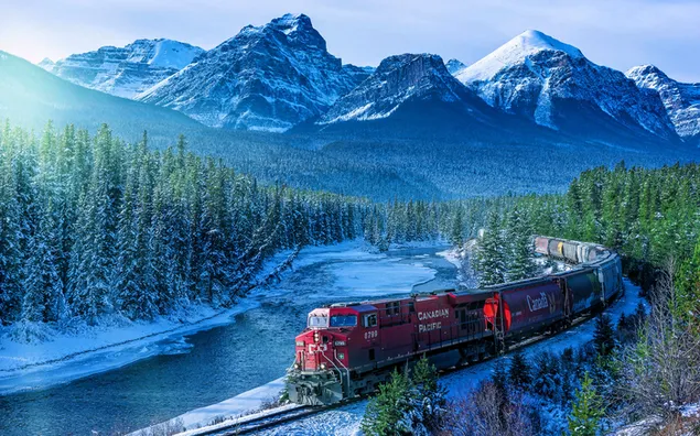 Red train leaving between snowy mountains and forests
