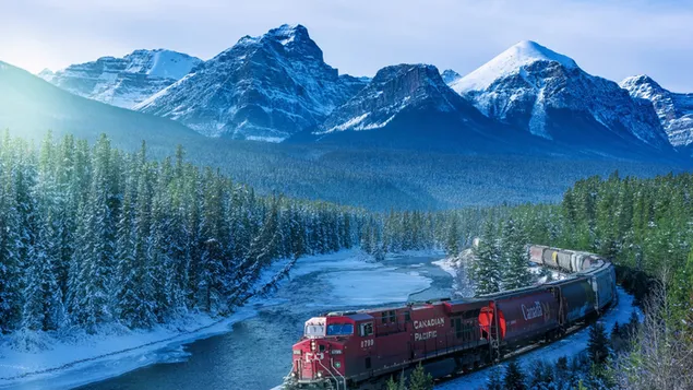 Vía roja del tren que pasa a través de montañas nevadas y bosques descargar
