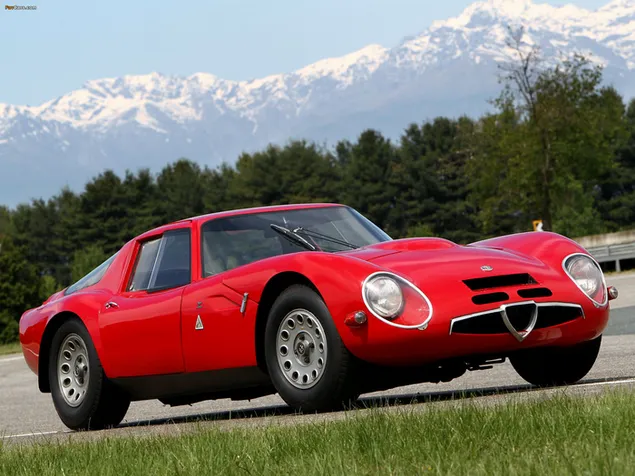 Rode vintage Alfa Romeo in besneeuwde bergen en groen veld download