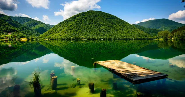 Reflejo de cielo nublado, camino de madera y montañas en agua clara natural