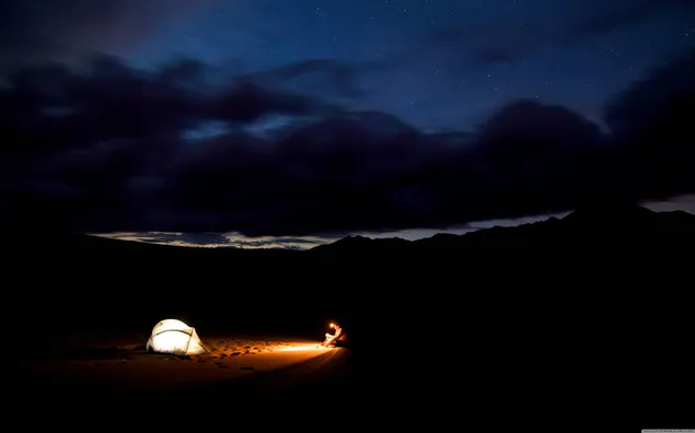 Reiziger die 's nachts kampeert onder blauwe lucht en zwarte wolken en een boek leest met behulp van licht