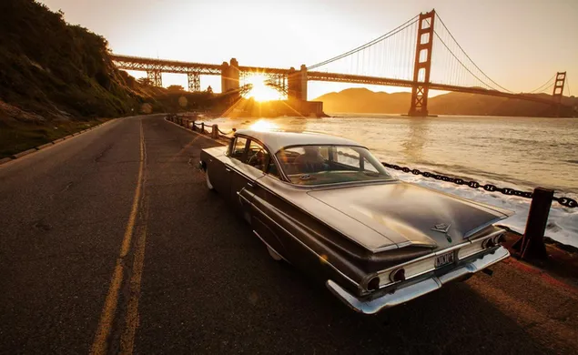 日没時に太陽が輝いて橋の後ろを運転している灰色のクラシックカー
