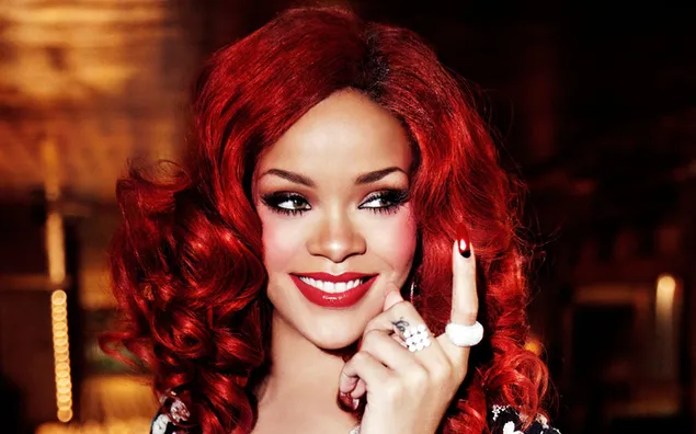 Rihanna lächelt, rotes Haar, Zeigefinger nach oben und Ringe an ihren Fingern
