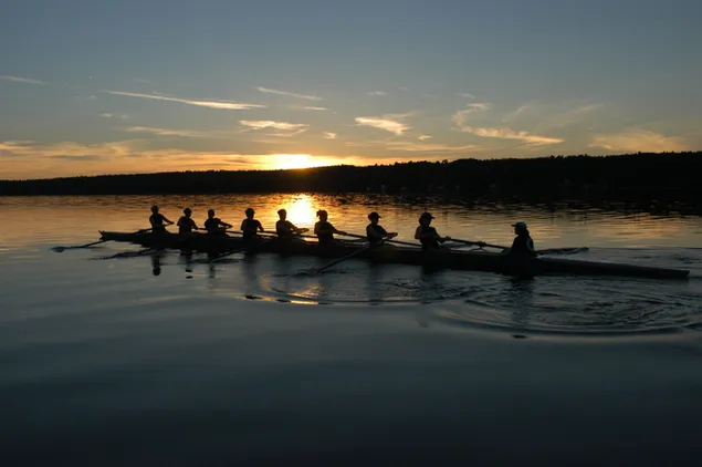 River silhouette of athletes rowing at sunset