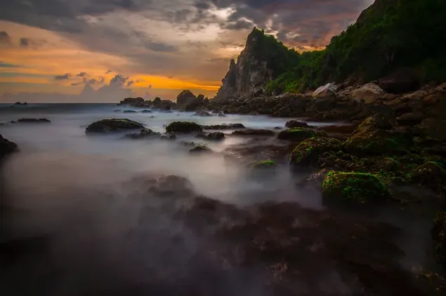 日没時の暗い雲の後ろの空の黄色のトーンの霧の中の岩や石 4K 壁紙