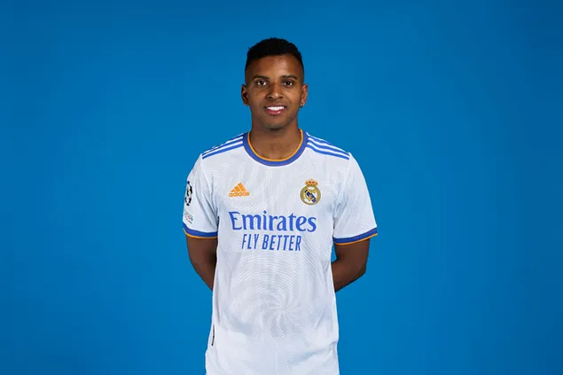 Rodrygo poseer met haar hande agter haar rug voor 'n blou agtergrond 2K muurpapier