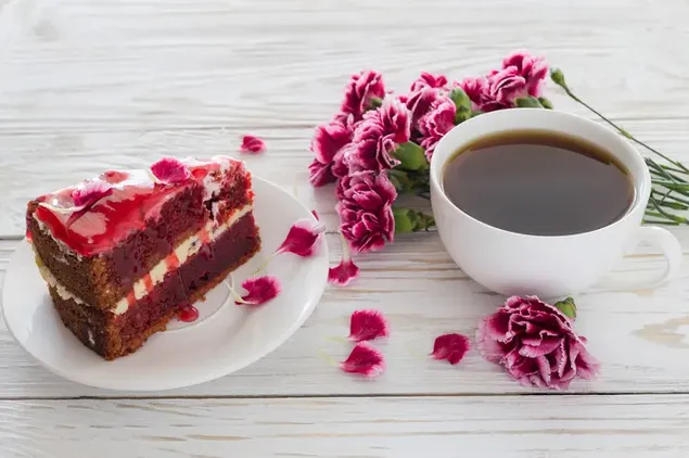 Pengaturan romantis dari sepotong kue beludru merah manis dengan teh dan bunga merah muda di sampingnya
