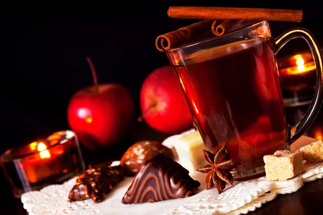 Rotweinglas mit roter Apfel- und Schokoladenpräsentation und Nelken obendrauf
