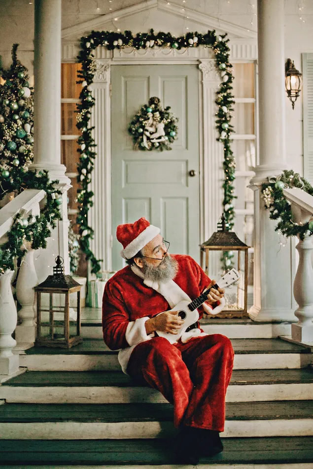 Santa bermain Ukulele di teras depan dengan latar belakang dekorasi Natal
