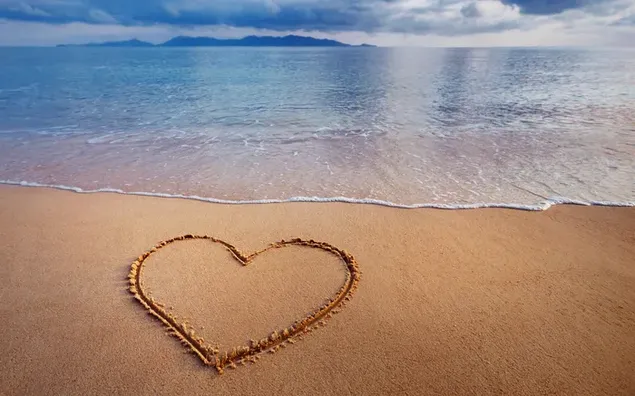 Zeegolven bereiken het hart getekend in het zand aan de kust download