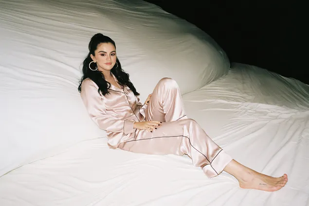 Selena Gomez liegt in ihrem hellrosa Satinpyjama auf dem großen Bett