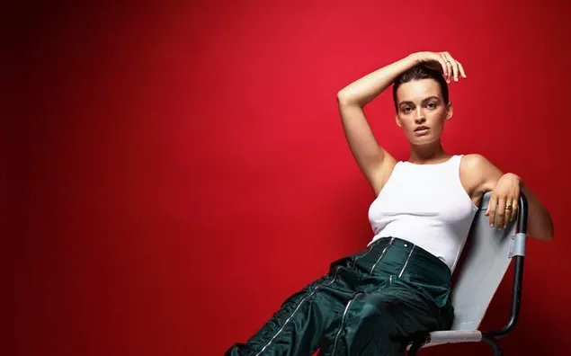 性感美麗的法英女演員艾瑪·​​麥基（Emma Mackey）身著白色背心和紅色背景的綠色褲子 4K 壁紙